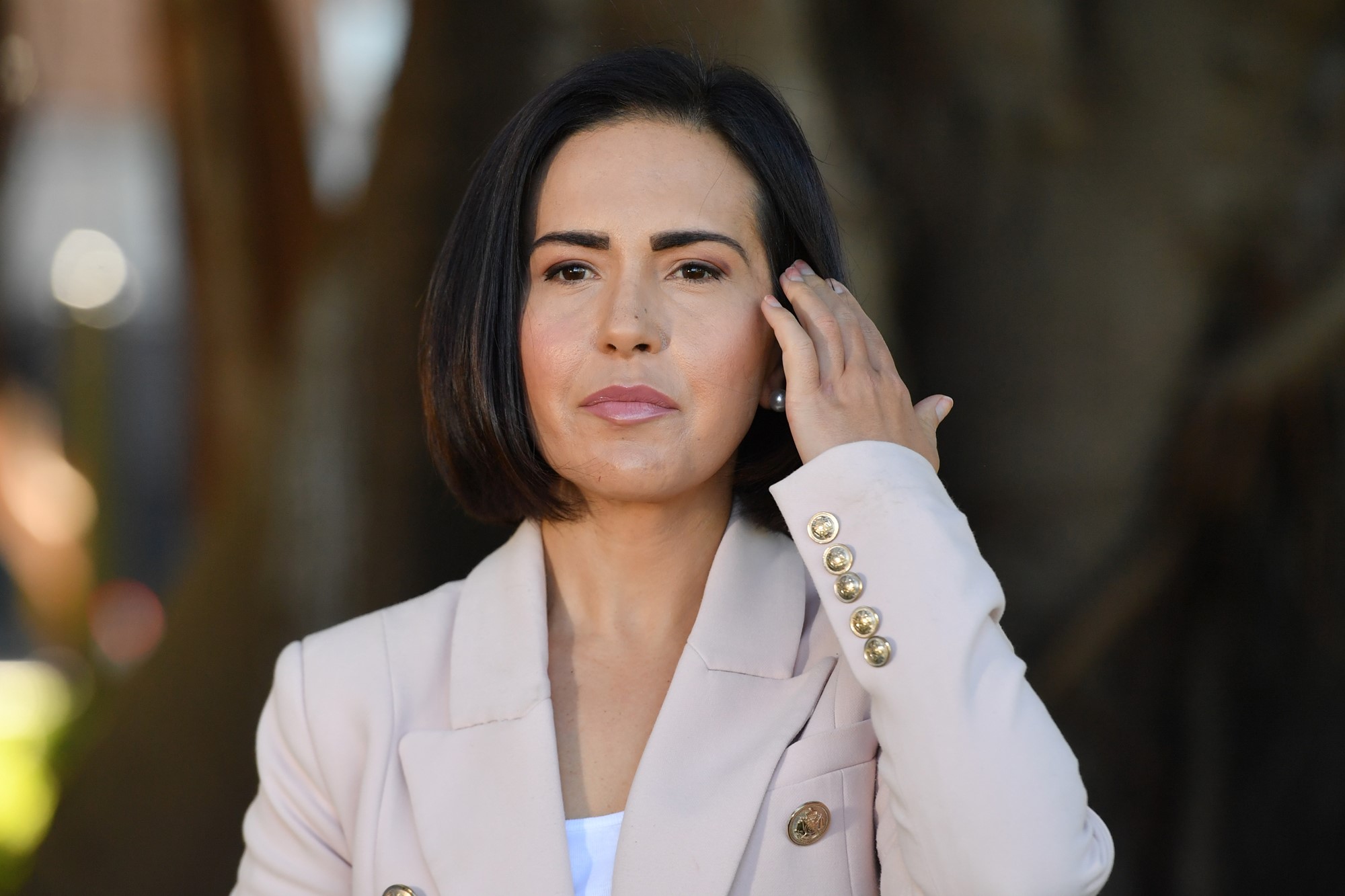 Woman with short dark bob and pink jacket touches hair