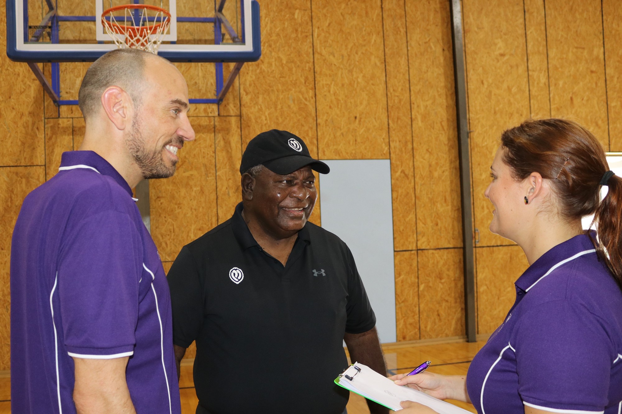 Benny Mills (centre) speaks to two people on a basketball court.