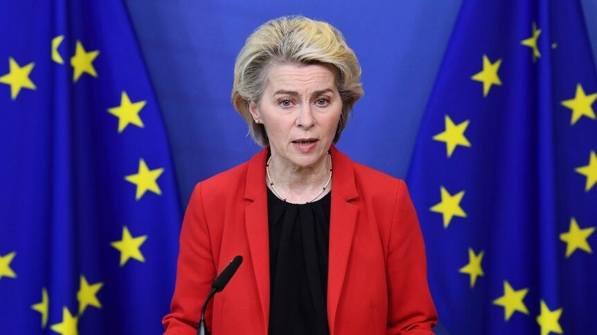 Ursula speaks at a conference in front of two European Union flags.