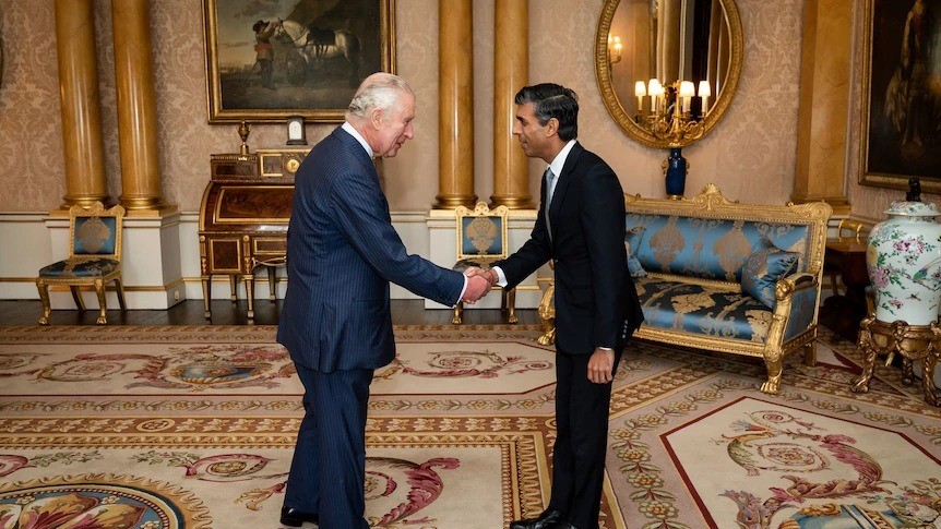 King Charles and Rishi Sunak shake hands in a grandiose room.