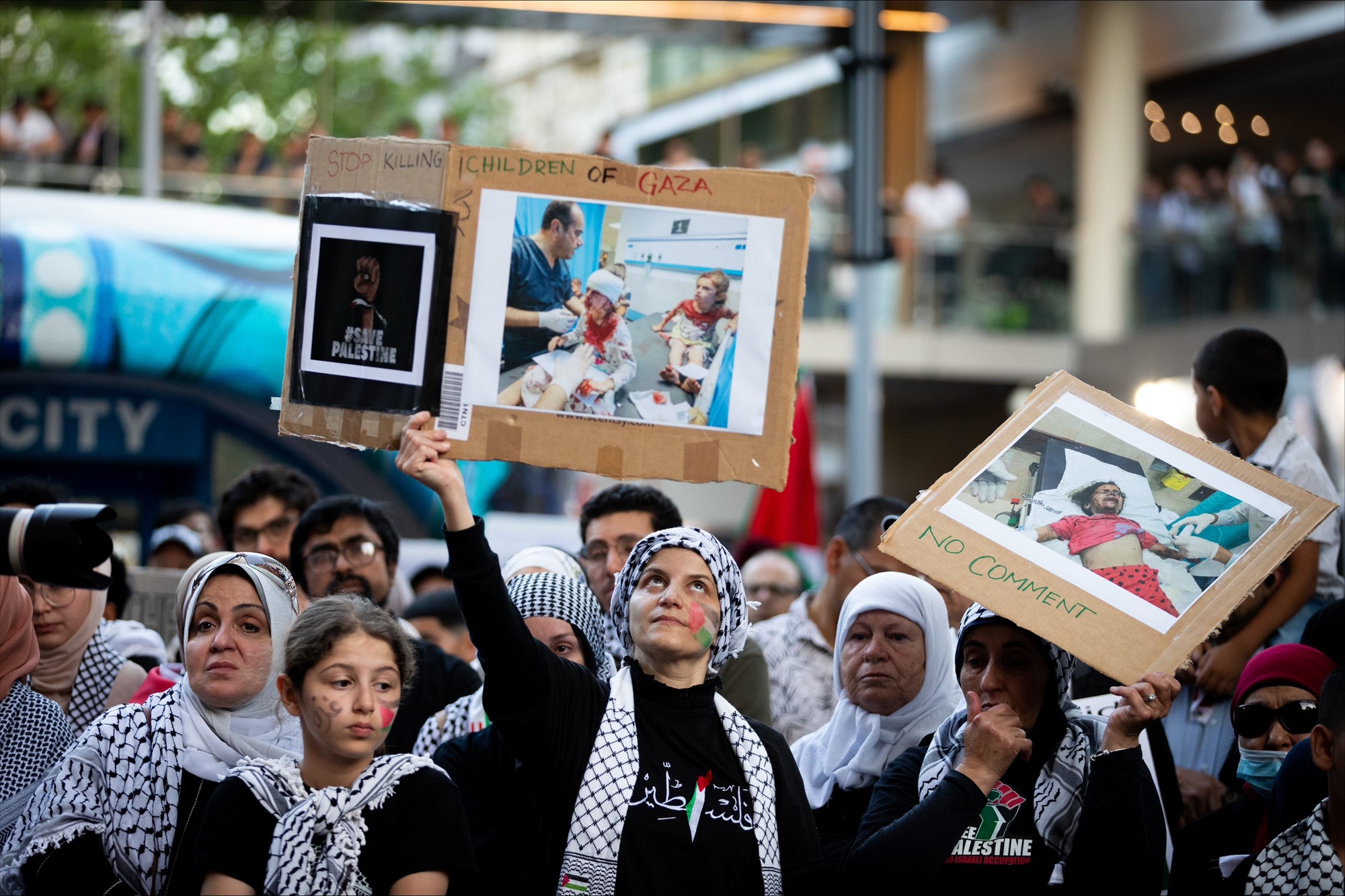 Women holding pictures of injured people up in a crowd. 