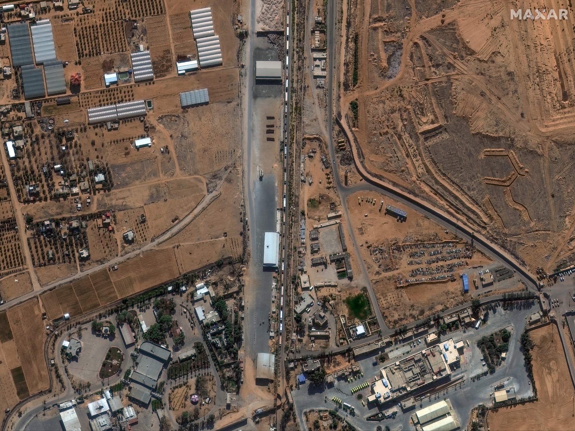 A satellite image shows a road lined with trucks, buildings and fields can be seen on either side
