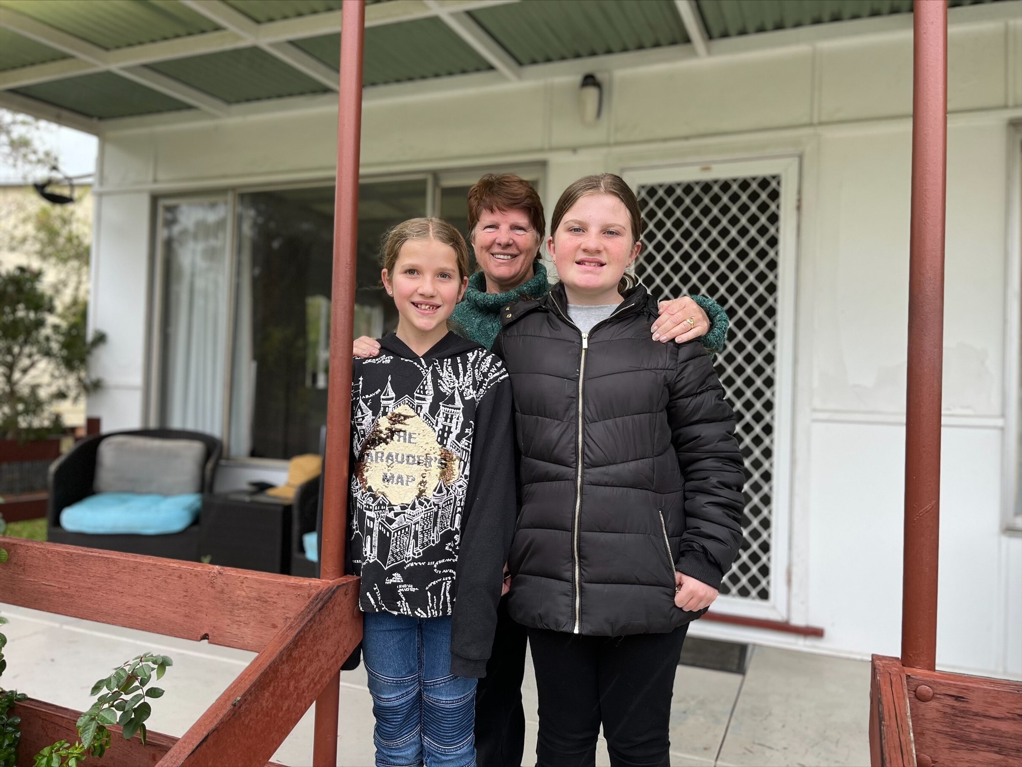 Stella Kelly and her two granddaughers stand on her verandah.
