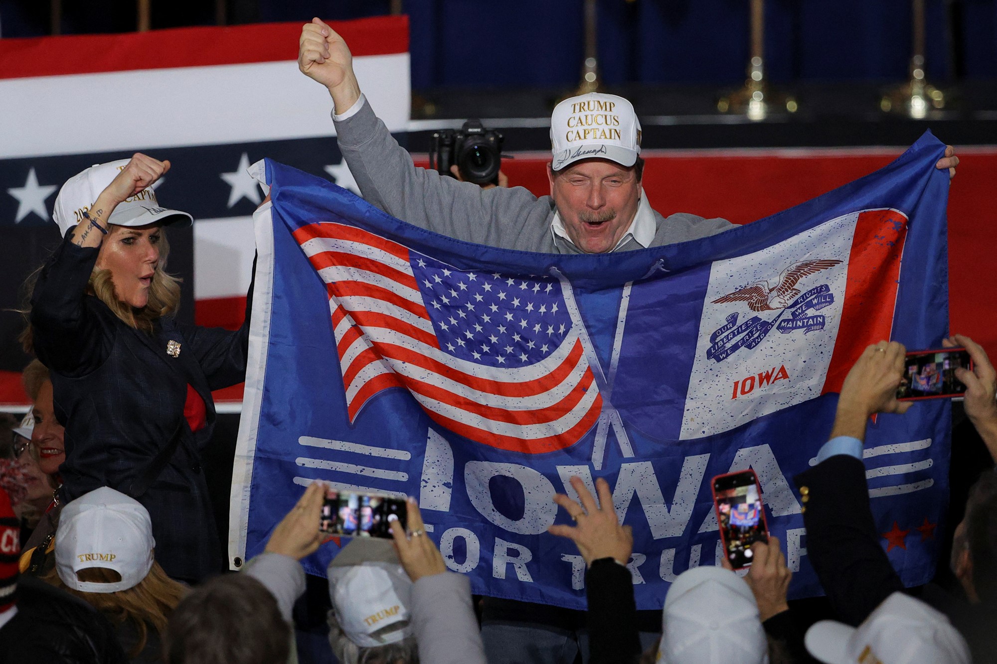 A man yells with joy while waving a blue IOWA FOR TRUMP flag
