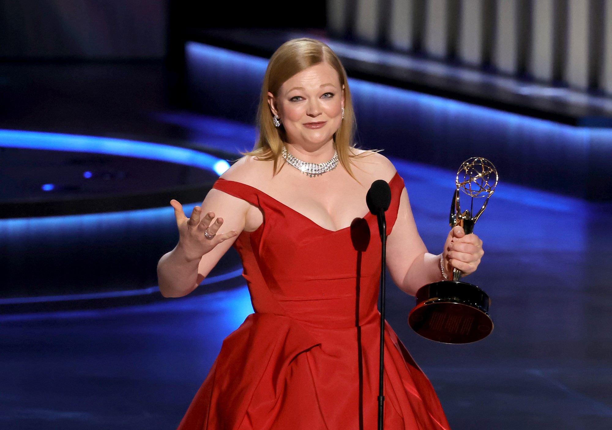 Sarah Snook with her arms out in a red dress.