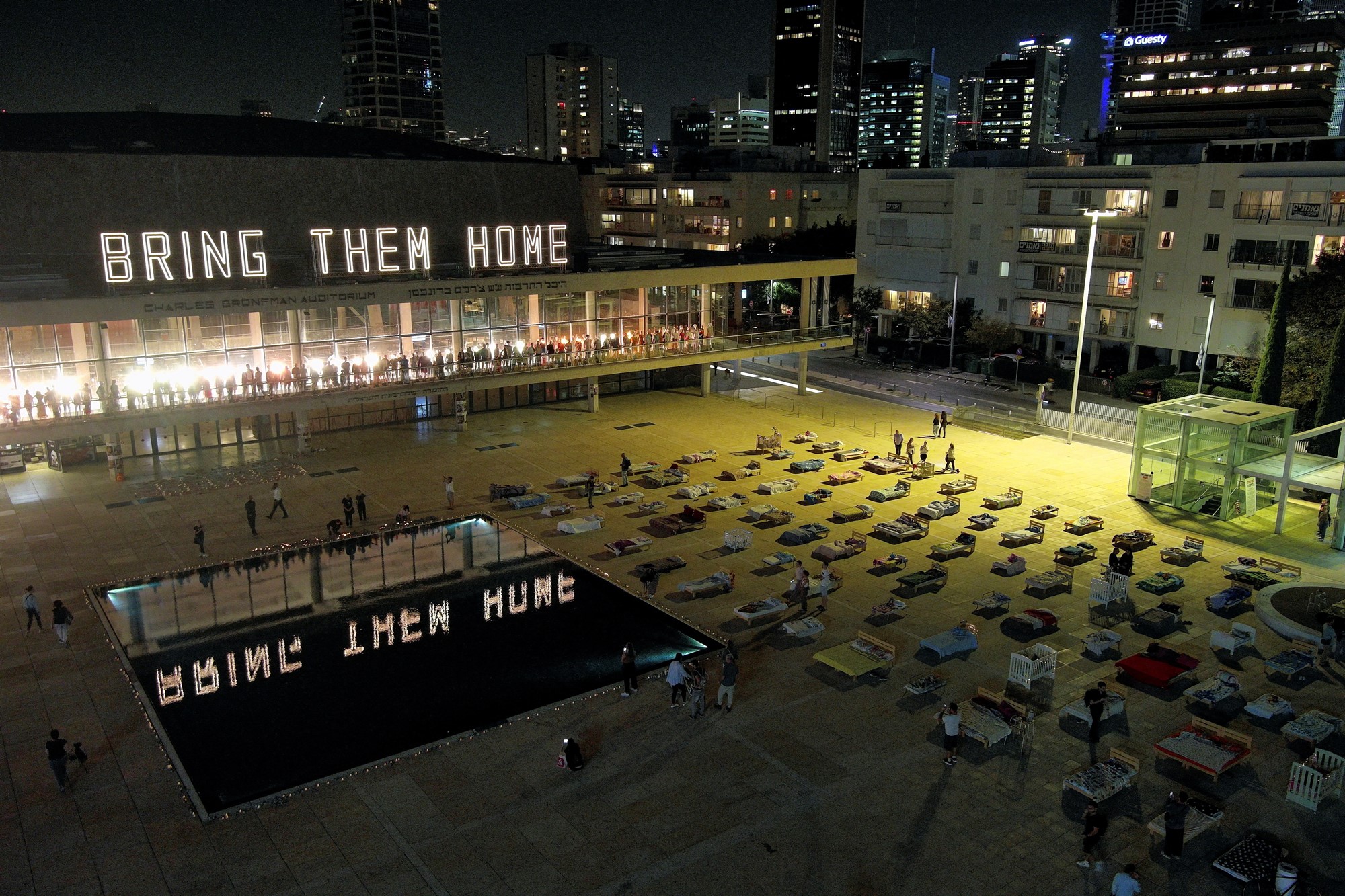 A high up view of beds displayed on a square with illuminated letters saying 'bring them home'