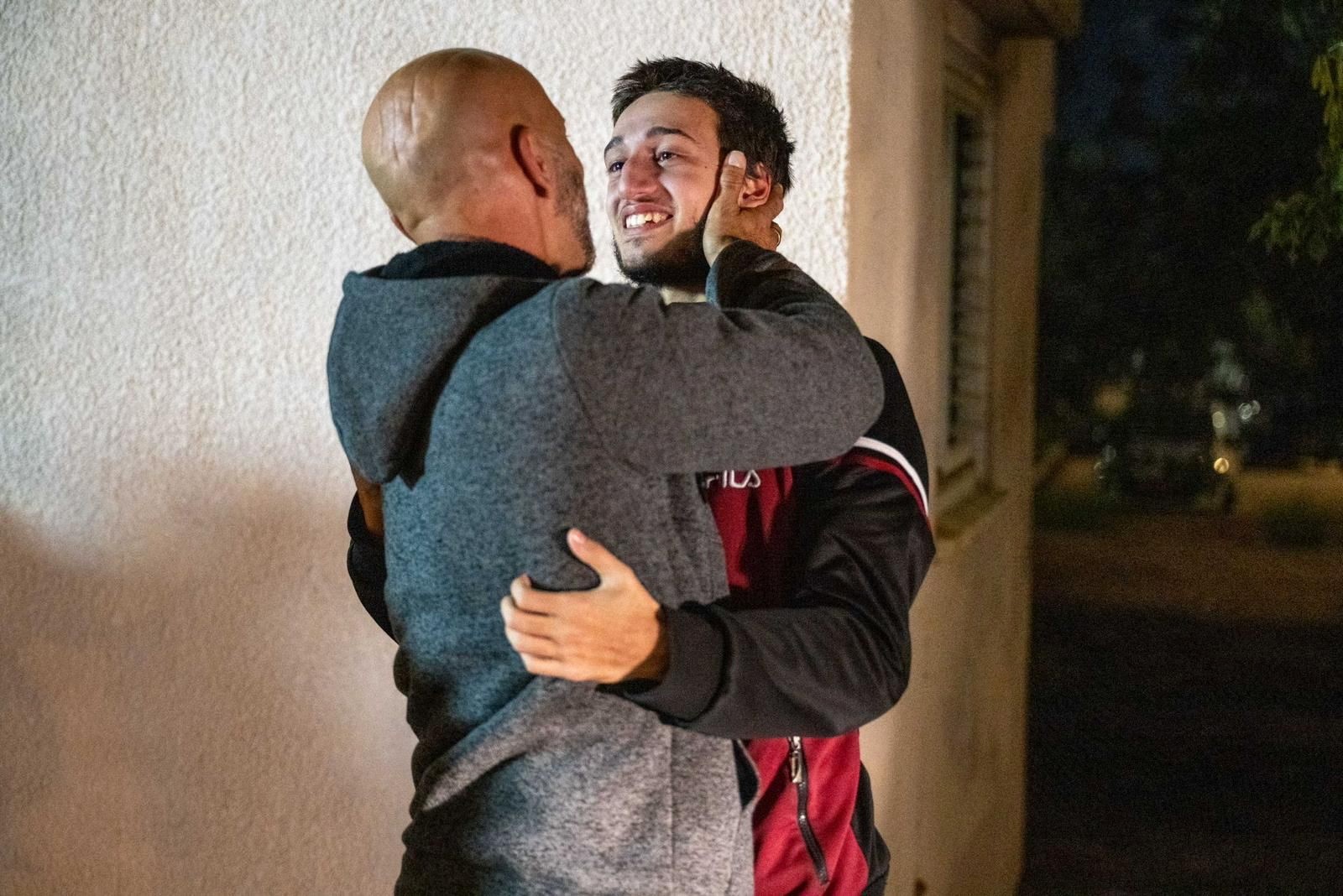 A young man looks at his father smiling as they embrace