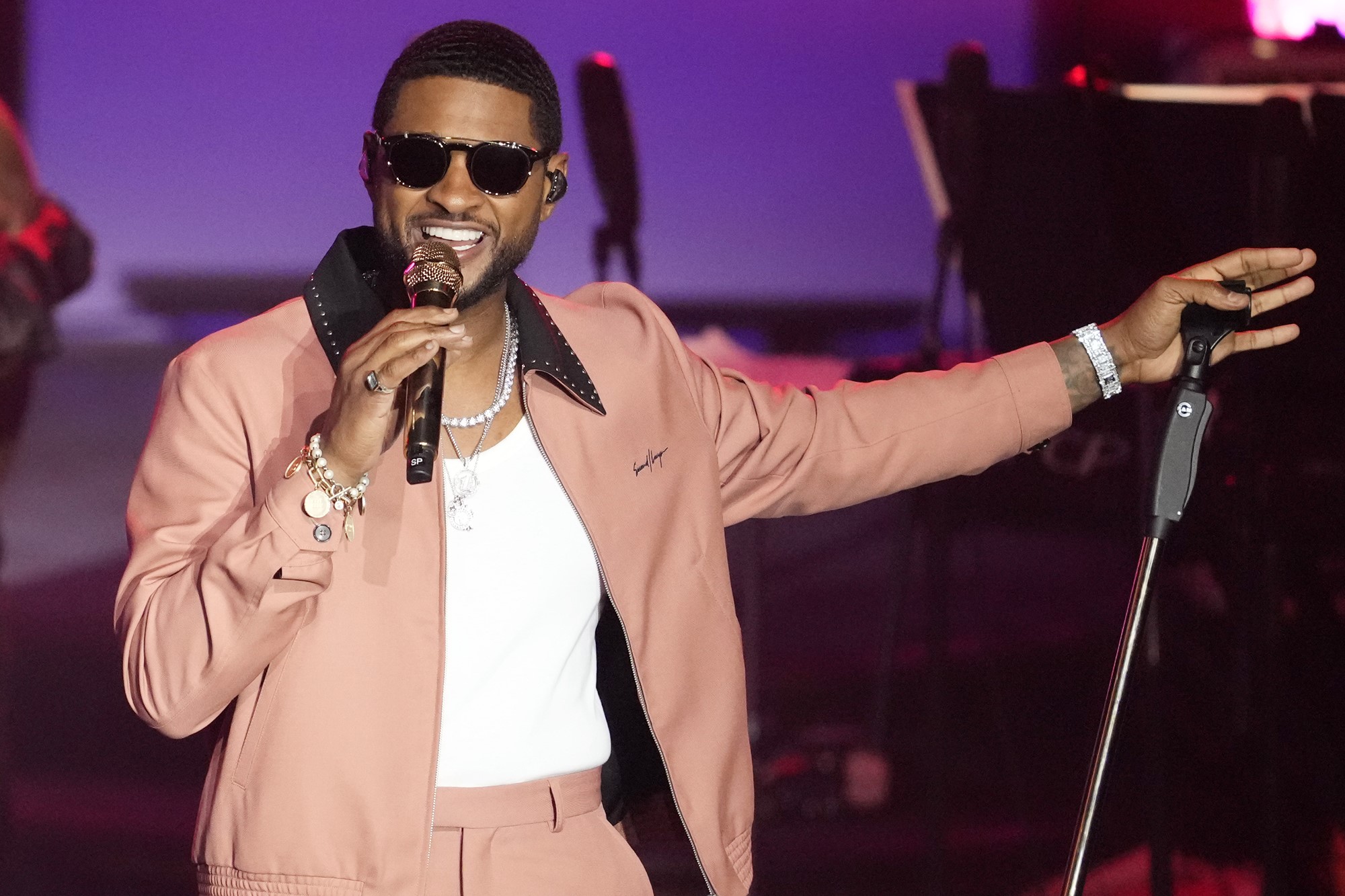 Usher smiles on stage as he sings into a microphone.