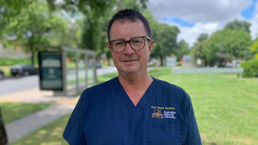 A middle-aged man with glasses outside in a blue medical uniform.