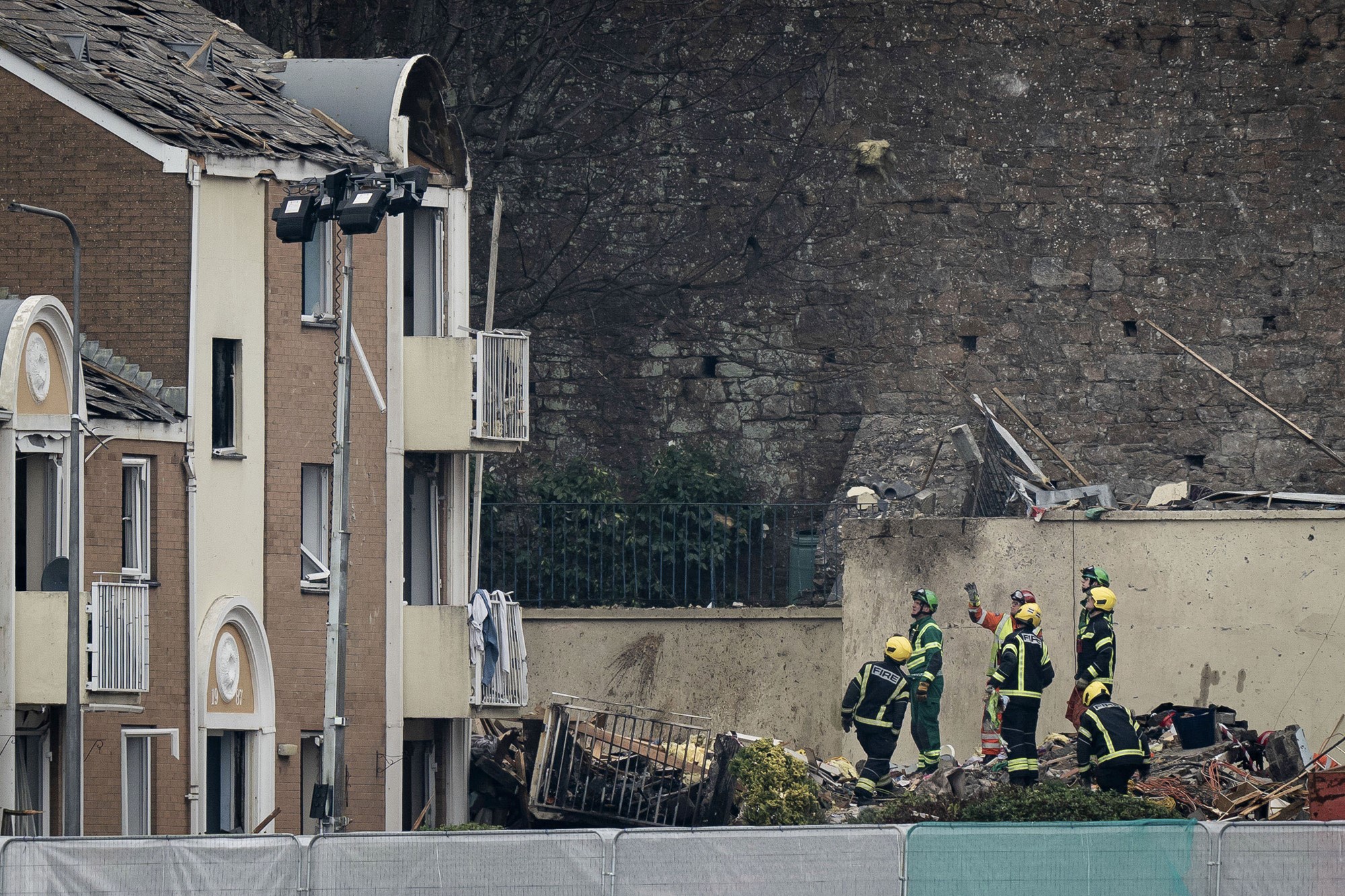 People in high vis emergency gear stand next to a damaged apartment building.