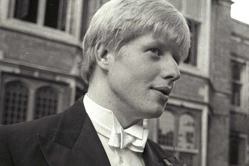 Close up of a young Boris Johnson wearing a suit, he looks to be in his early 20s.