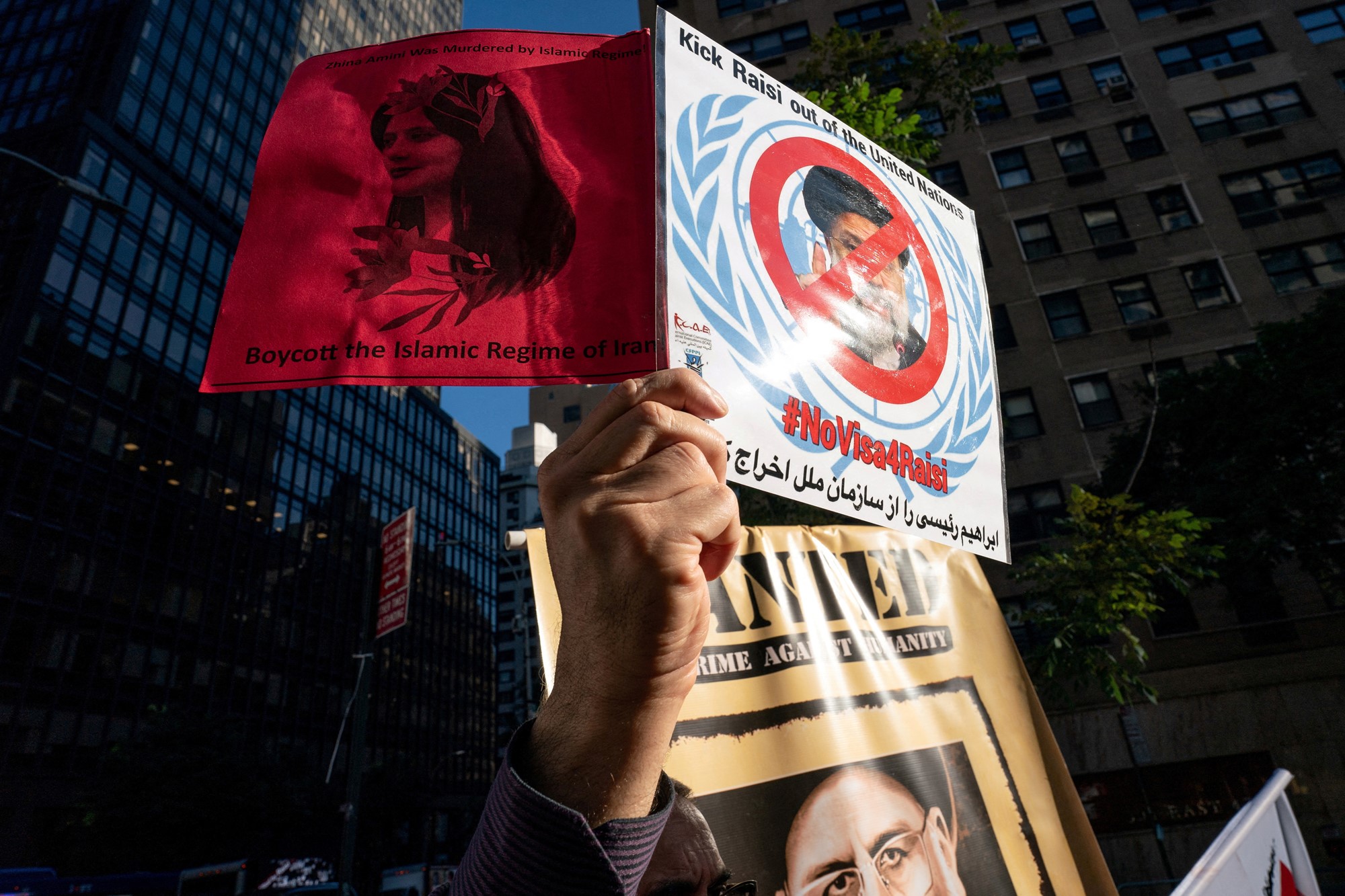 a person holds up a sign at a protest that says 'kick raisi out of the united nations'