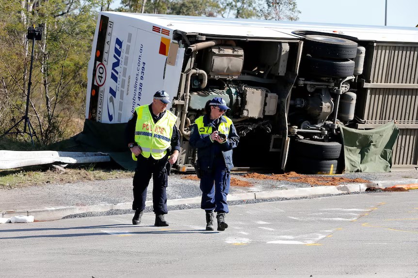 Two police stand near an overturned bus on the side of a road