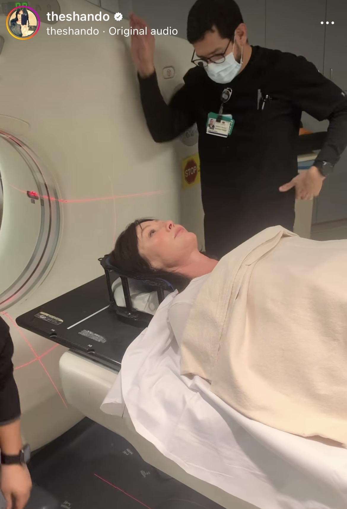 Shannen Dohety laying down on a stretcher before receiving radiation therapy. A medical professional is standing over her.