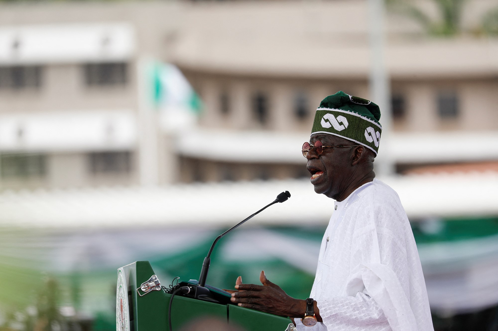 Bola Tinubu dressed in white at a microphone. 