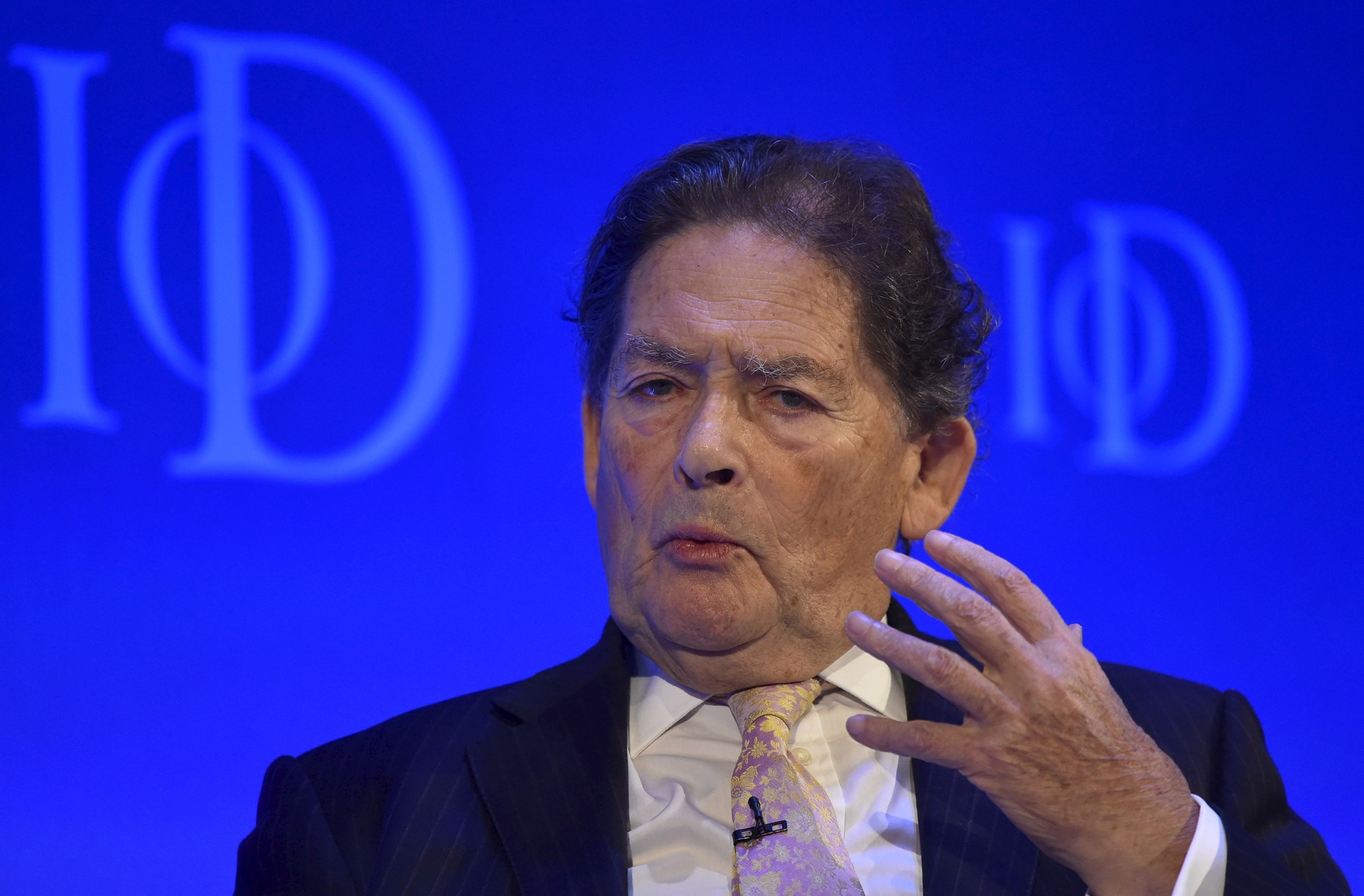 Nigel Lawson, wearing a suit, speaks and gestures with a hand