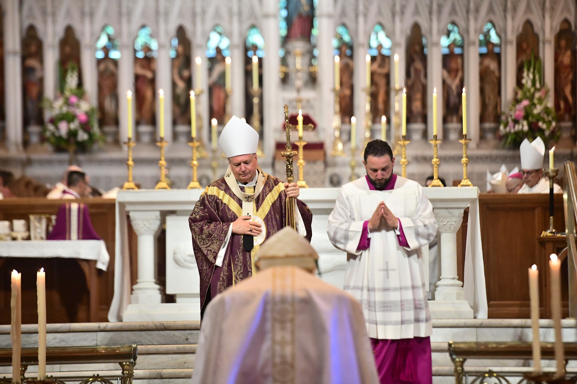 Two men wearing religious gowns stand at the front of a mass service.