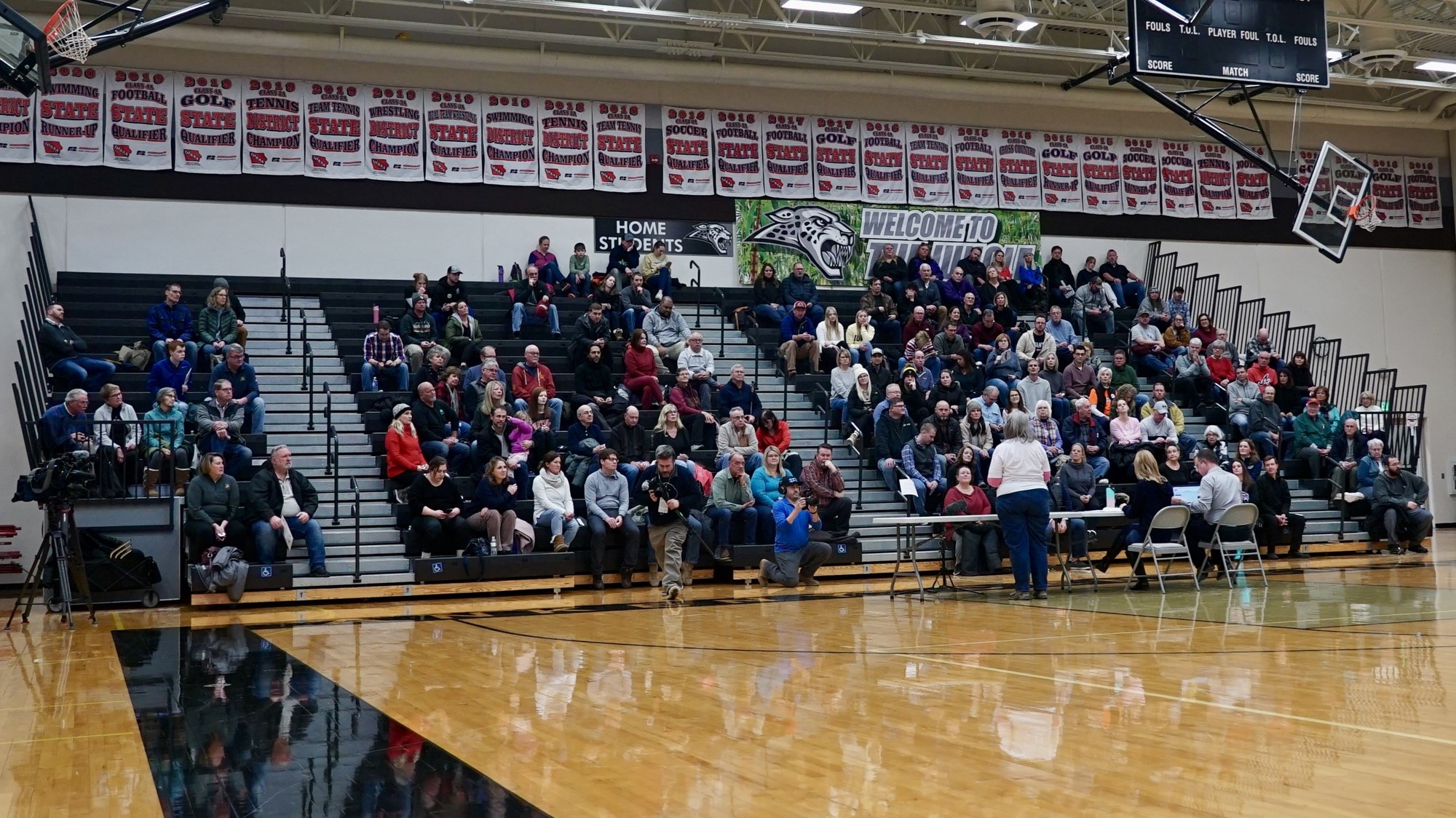 People sit in the stands at an indoor basketball court.