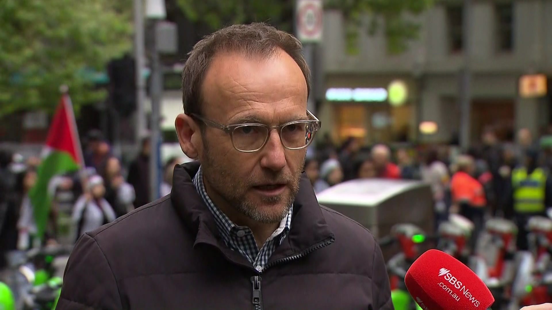 Adam Bandt speaks to microphones in front of a crowd of pro-Palestinian protesters