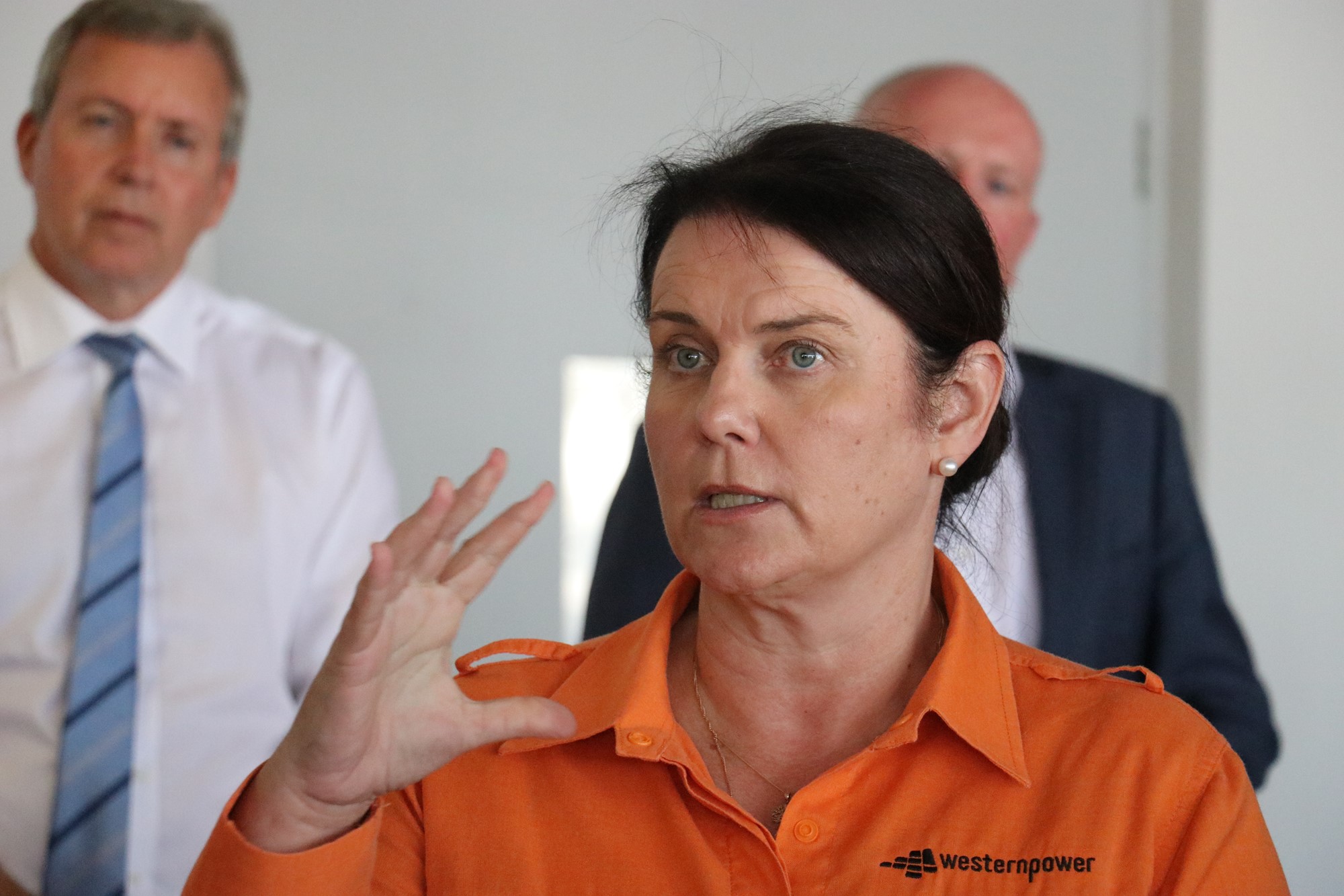A woman in an orange shirt speaks at a press conference