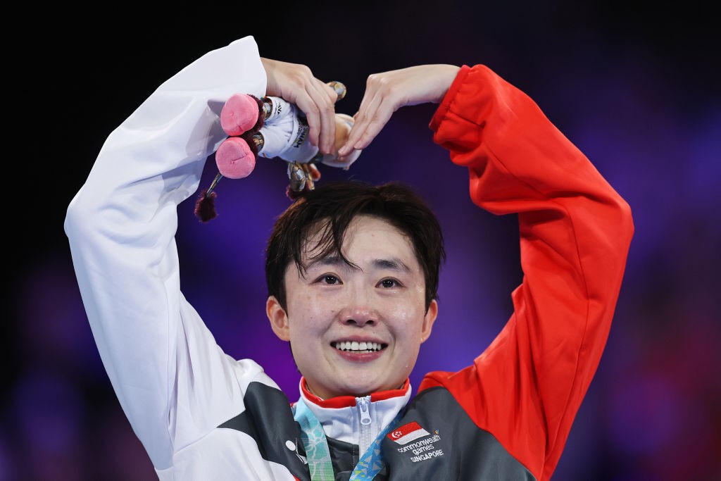 table tennis athlete smiles and holds arms up on podium