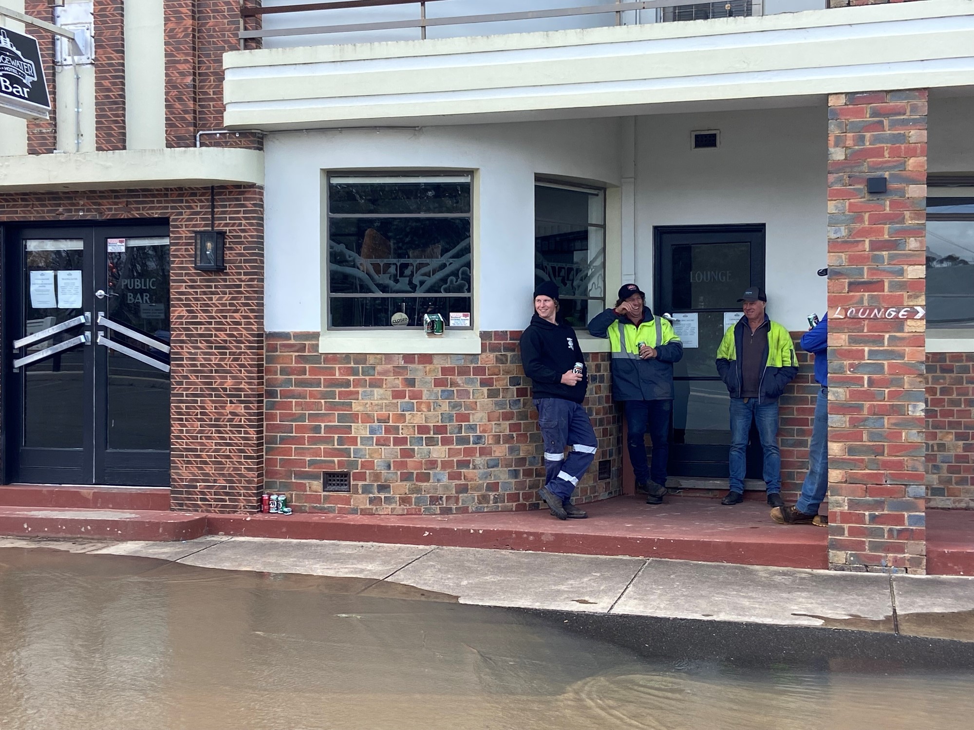 Three men outside a pub, surrounded by floodwater.
