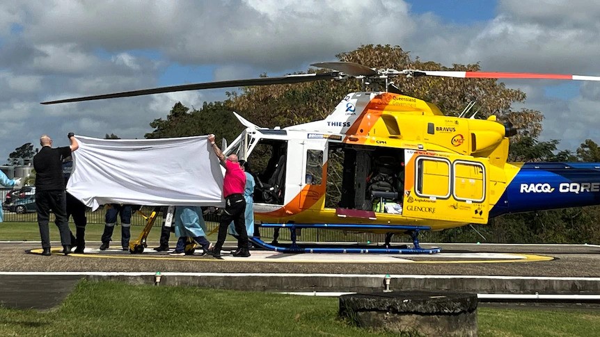 People hold a white sheet over a person being wheeled away from a helicopter on a stretcher