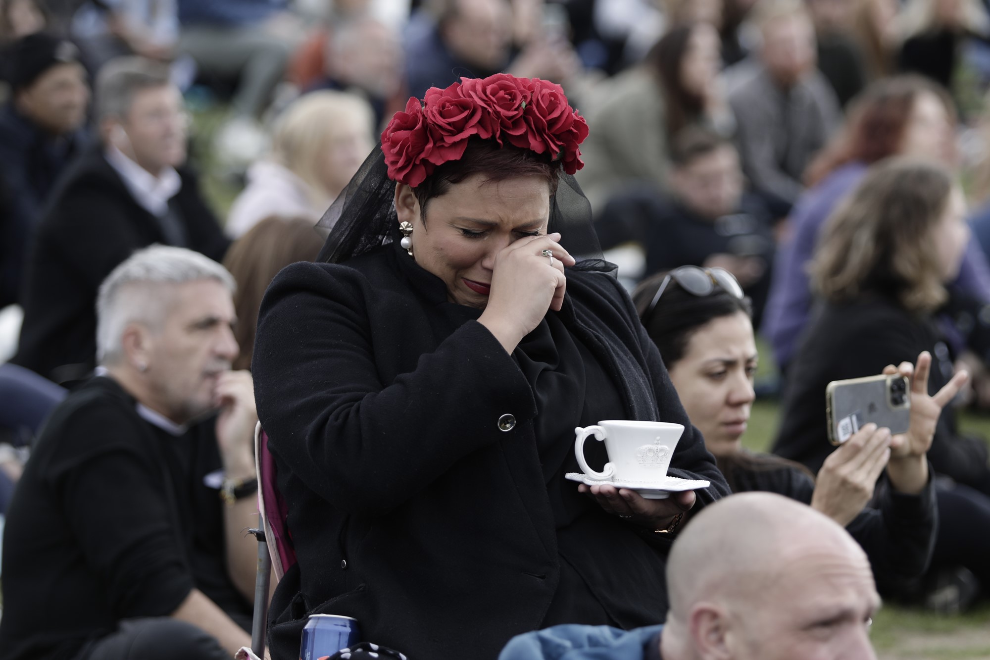 A woman sits crying while holding a cup of tea