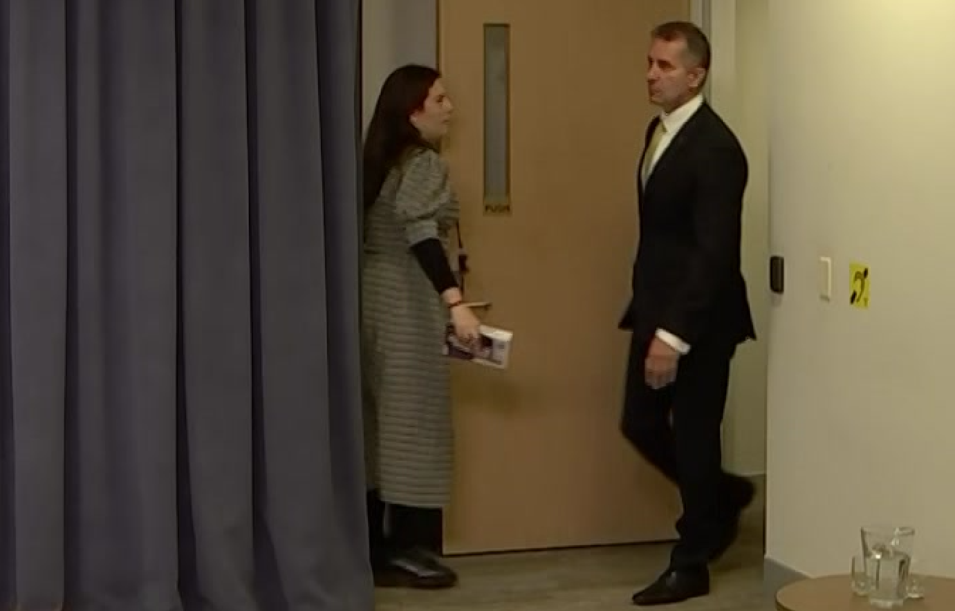 A person stands near a door clutching a box of tissues