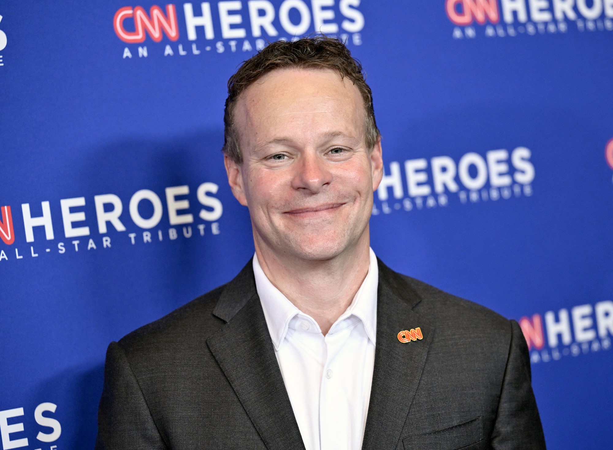 A white man with short hair smiles while wearing a suit with a CNN pin on it