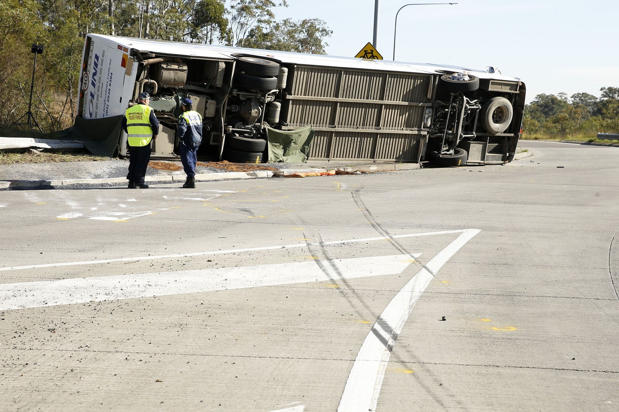 A large bus on its side next to a road, with skid marks and police nearby