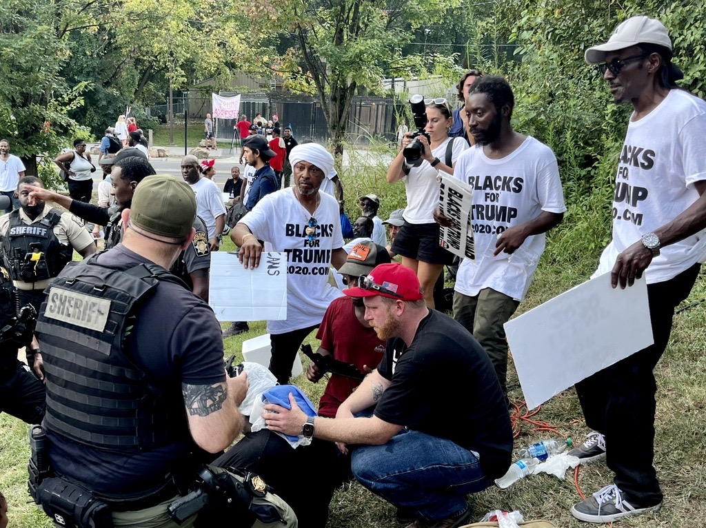 A man is attended to by a sheriff. Men wear shirts saying 'BLACKS FOR TRUMP'.