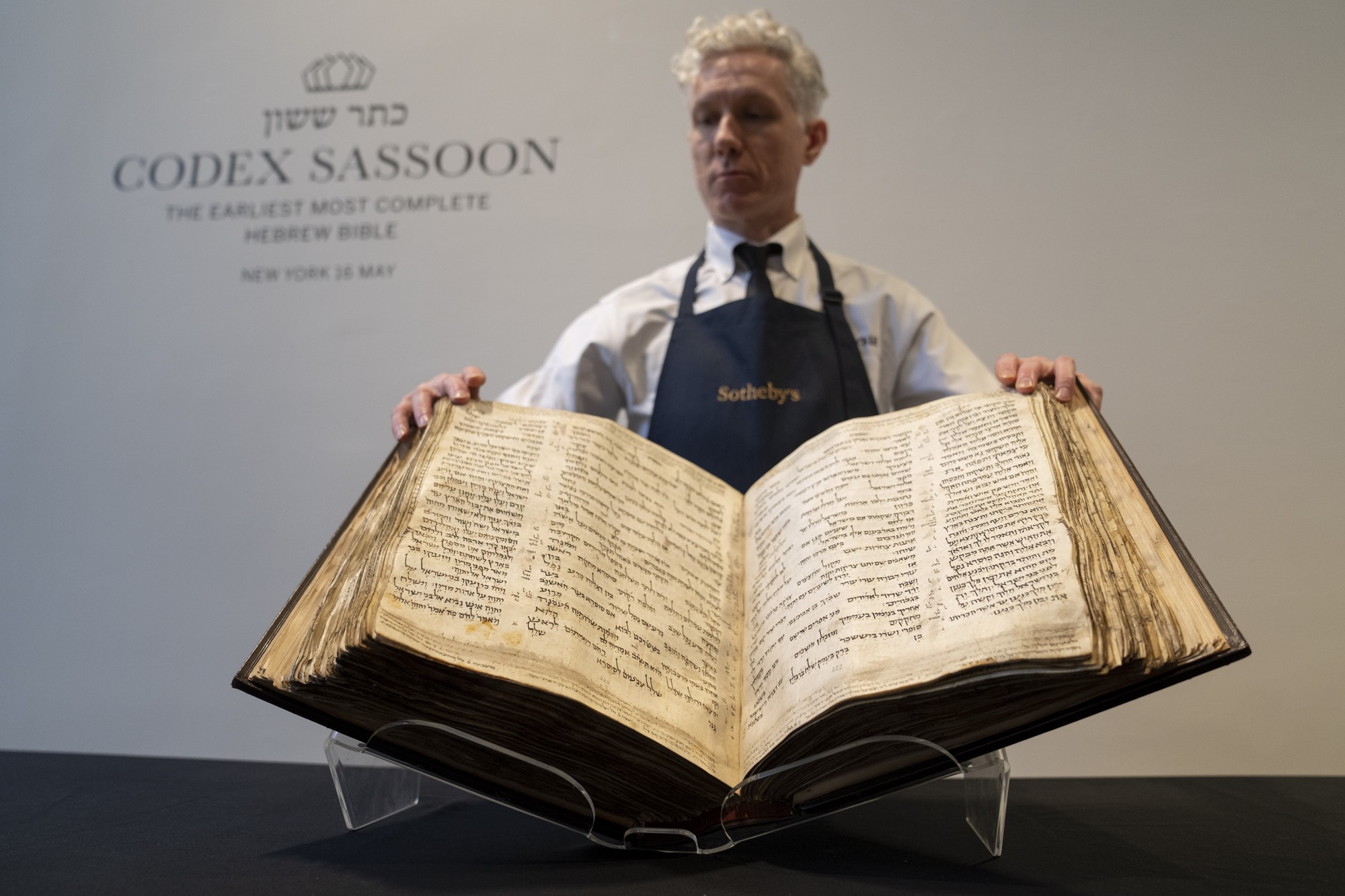 A man in an apron holds out a large, old book for display