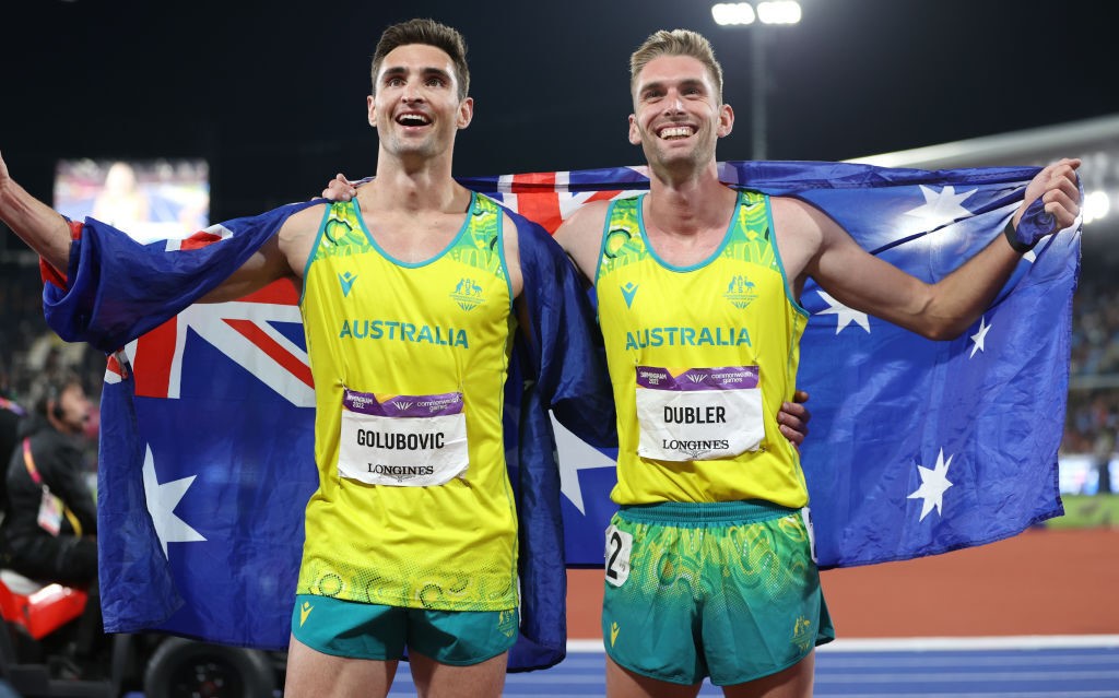 Two men smile with an Australian flag behind them
