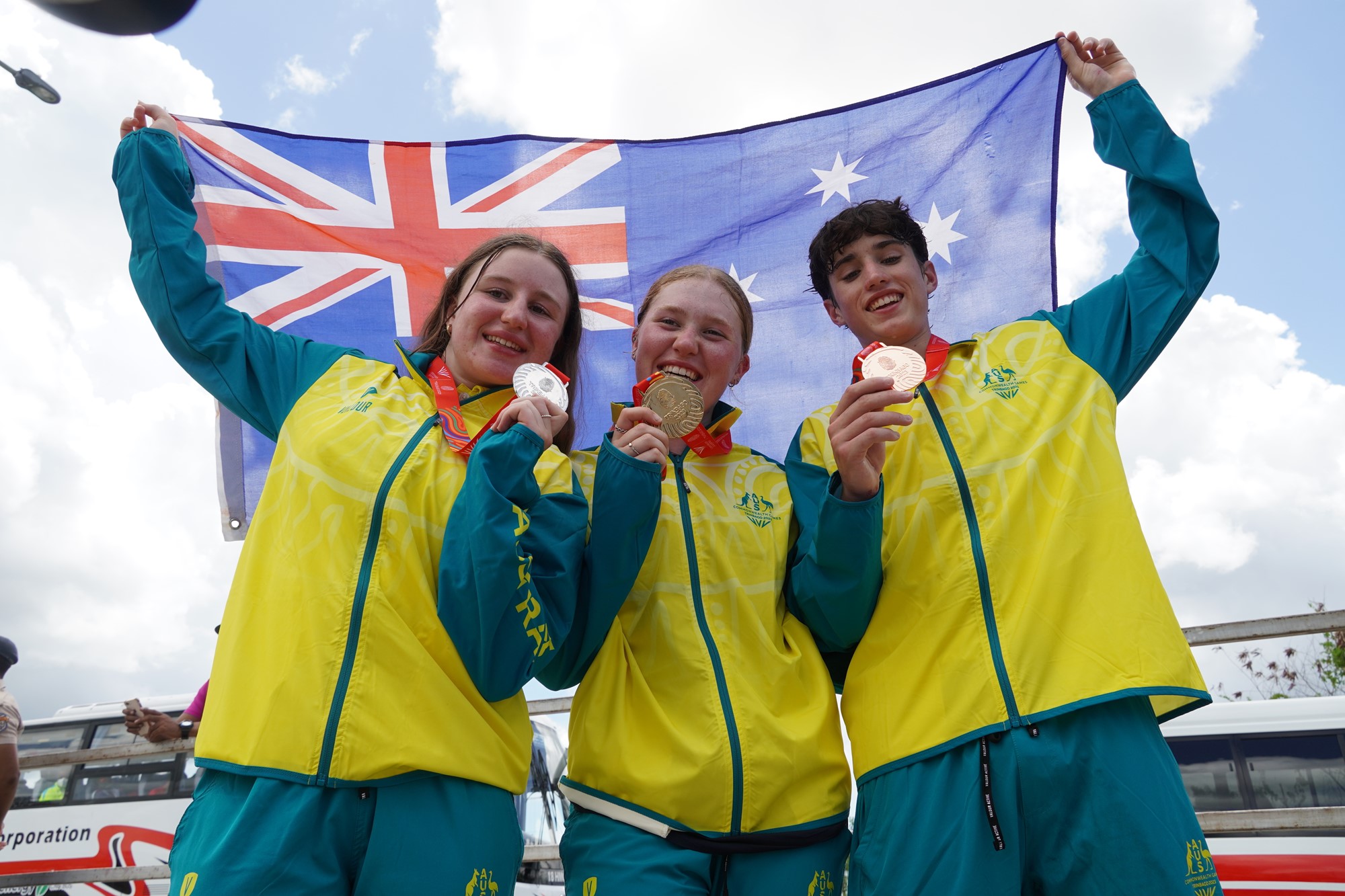 Three people in green and yellow jackets hold up medals