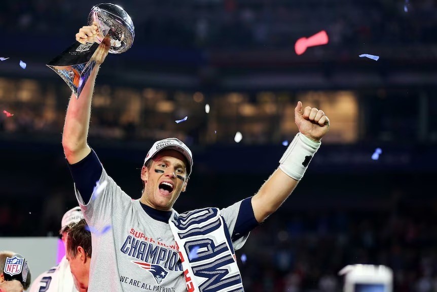 Tom Brady holds up a Super Bowl trophy.