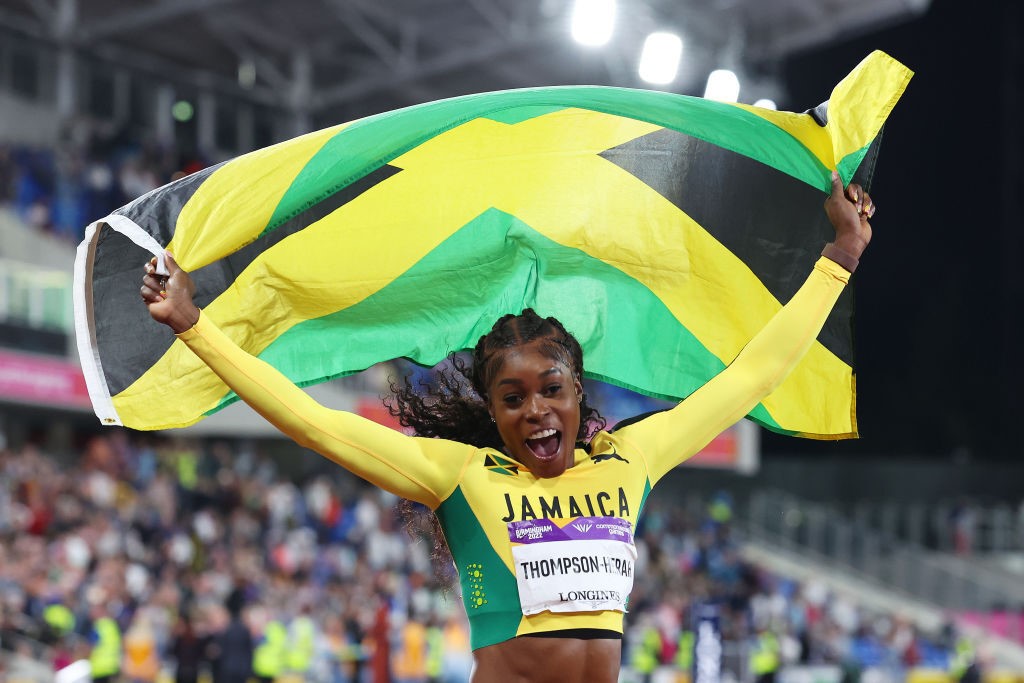 runner elaine thompson-herah waves the jamaican flag above her head while celebrating a win