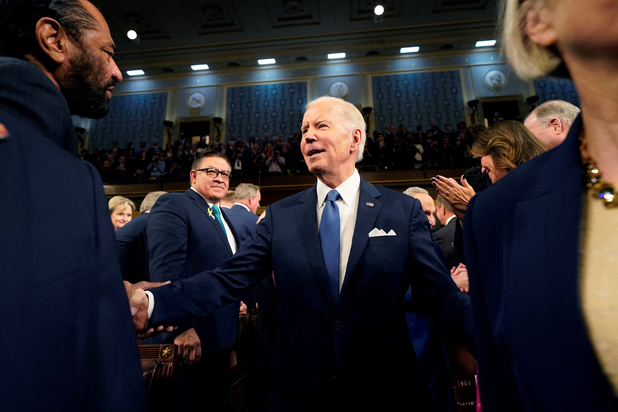 Biden shakes people's hands as he enters the chamber.