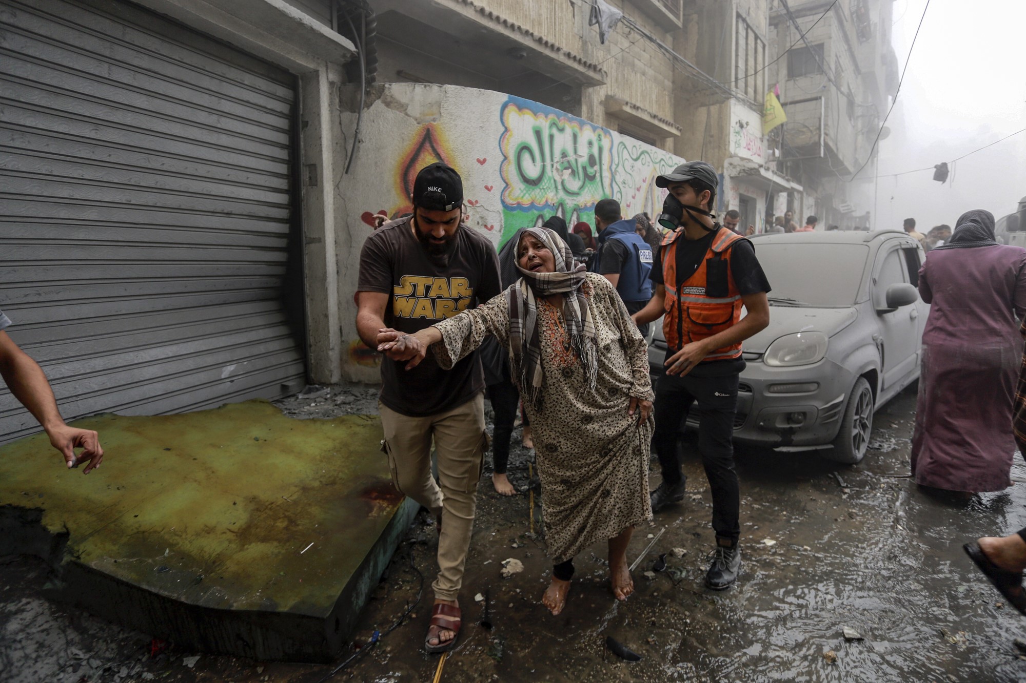 A woman is being led away by two men walking down a street filled wih water and debris
