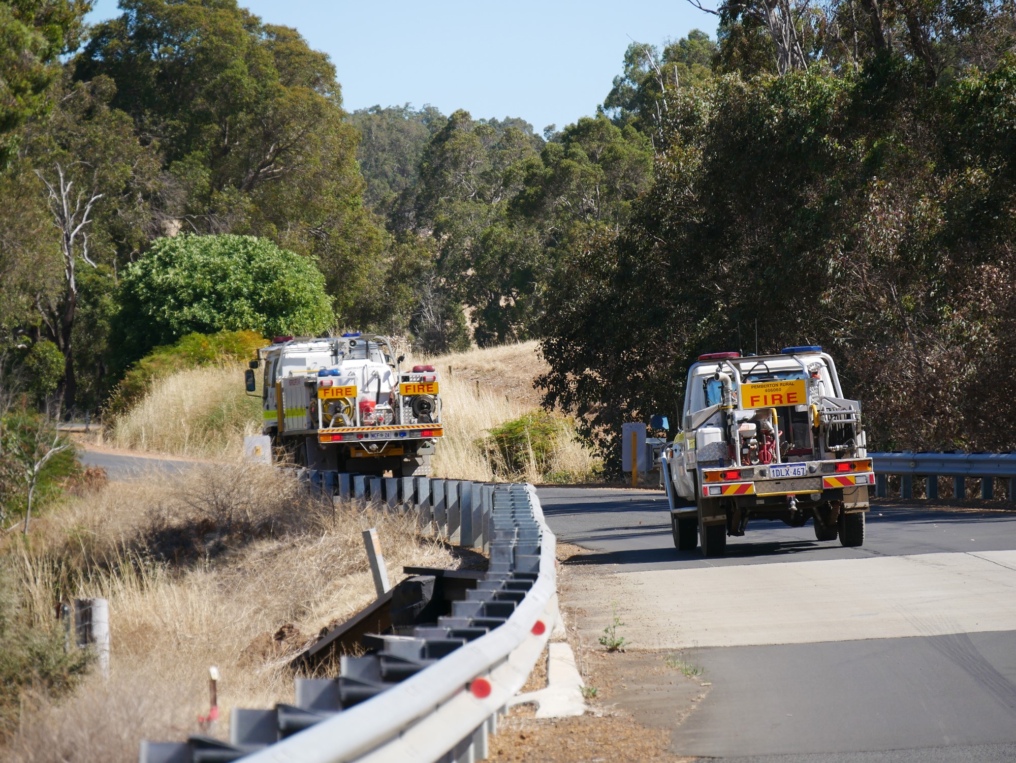 Two fire trucks drive towards bushland