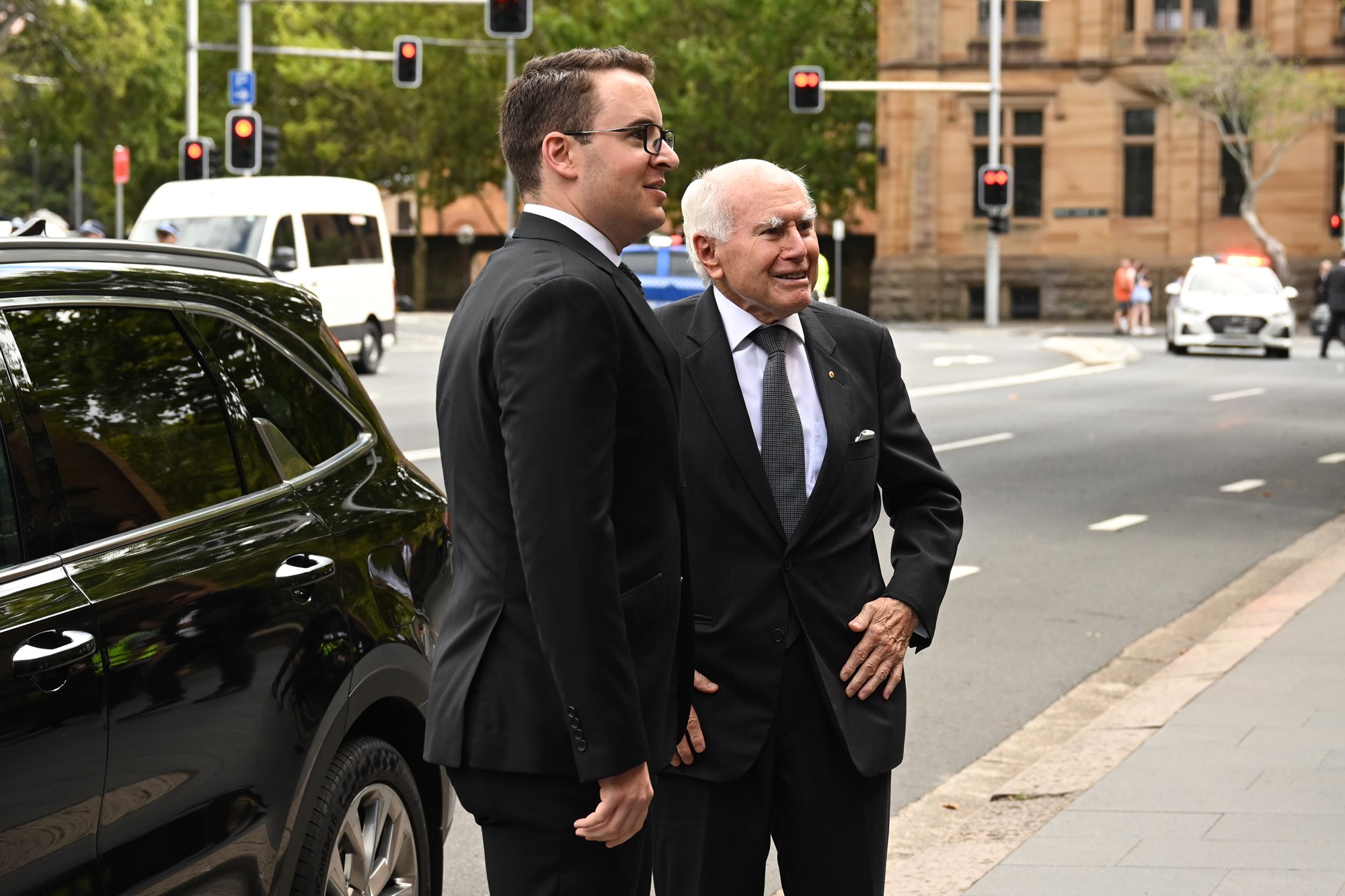 John Howard and another man stand in front of a black car