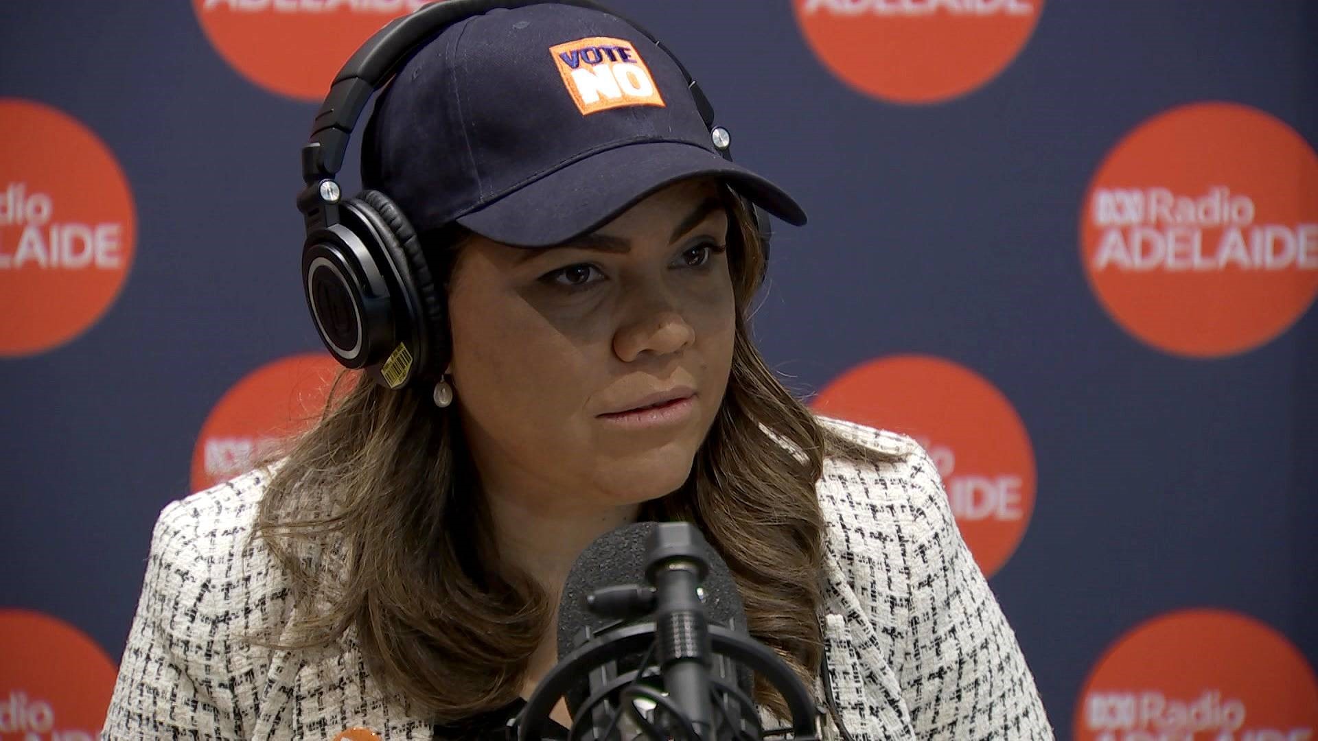 A woman wears a cap and headphones while speaking into a microphone.
