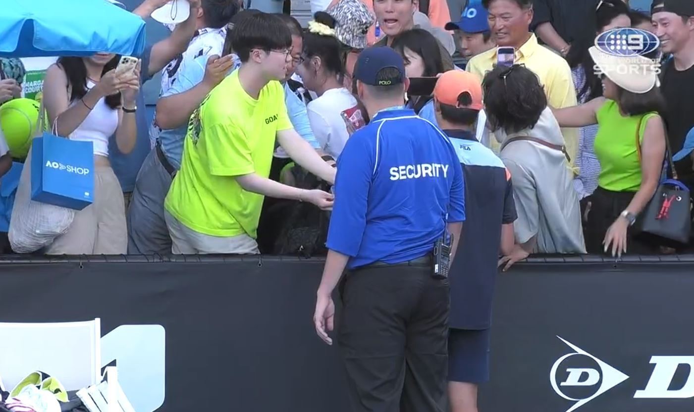 A tennis player signs autographs as security looks on.