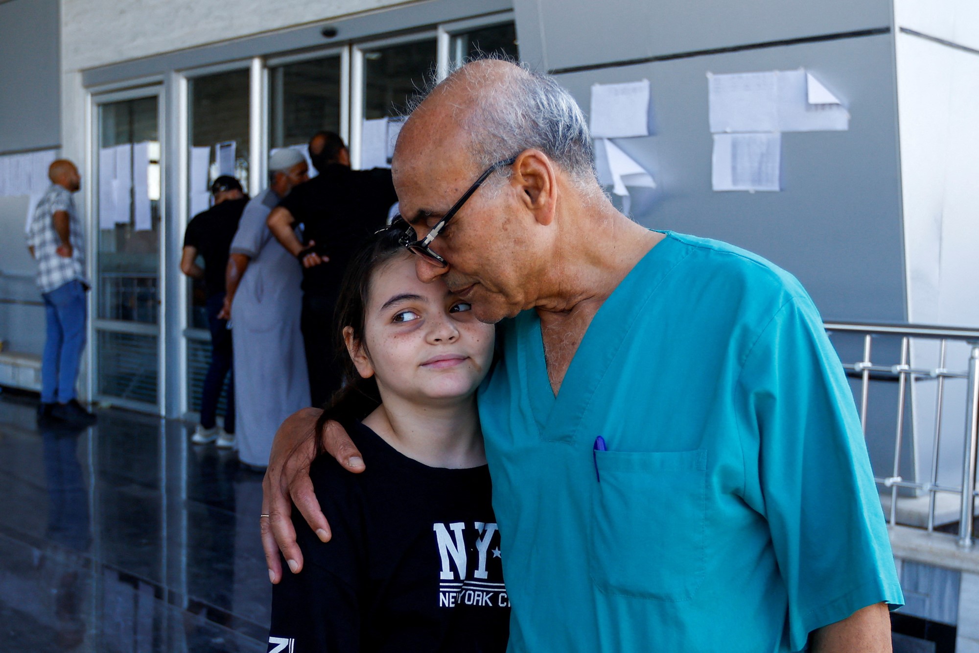 A man wearing doctor's scrubs puts his arm around his daughter
