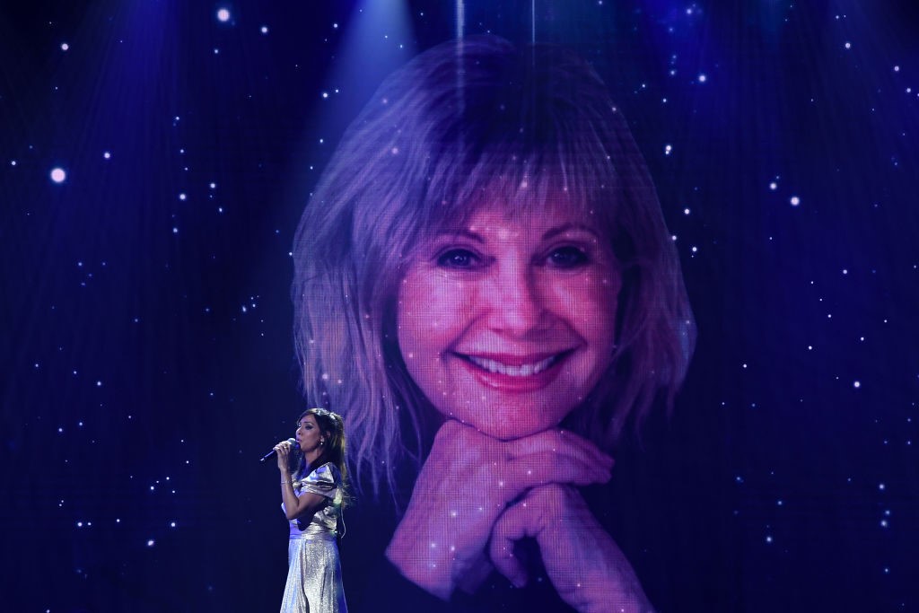natalie imbruglia sings in front of a big picture of olivia newton-john