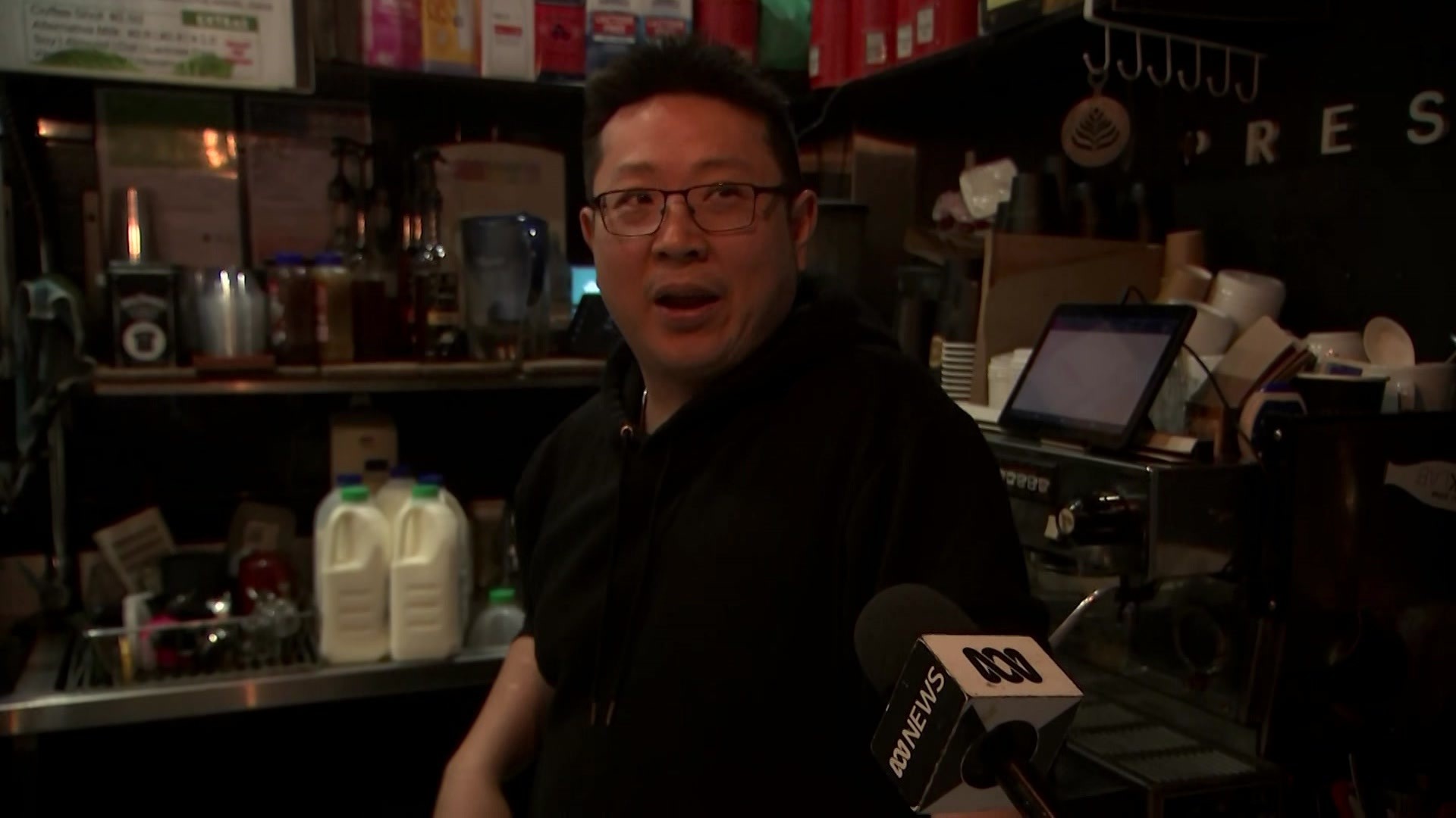 John Chen speaks into a microphone in a cafe kitchen