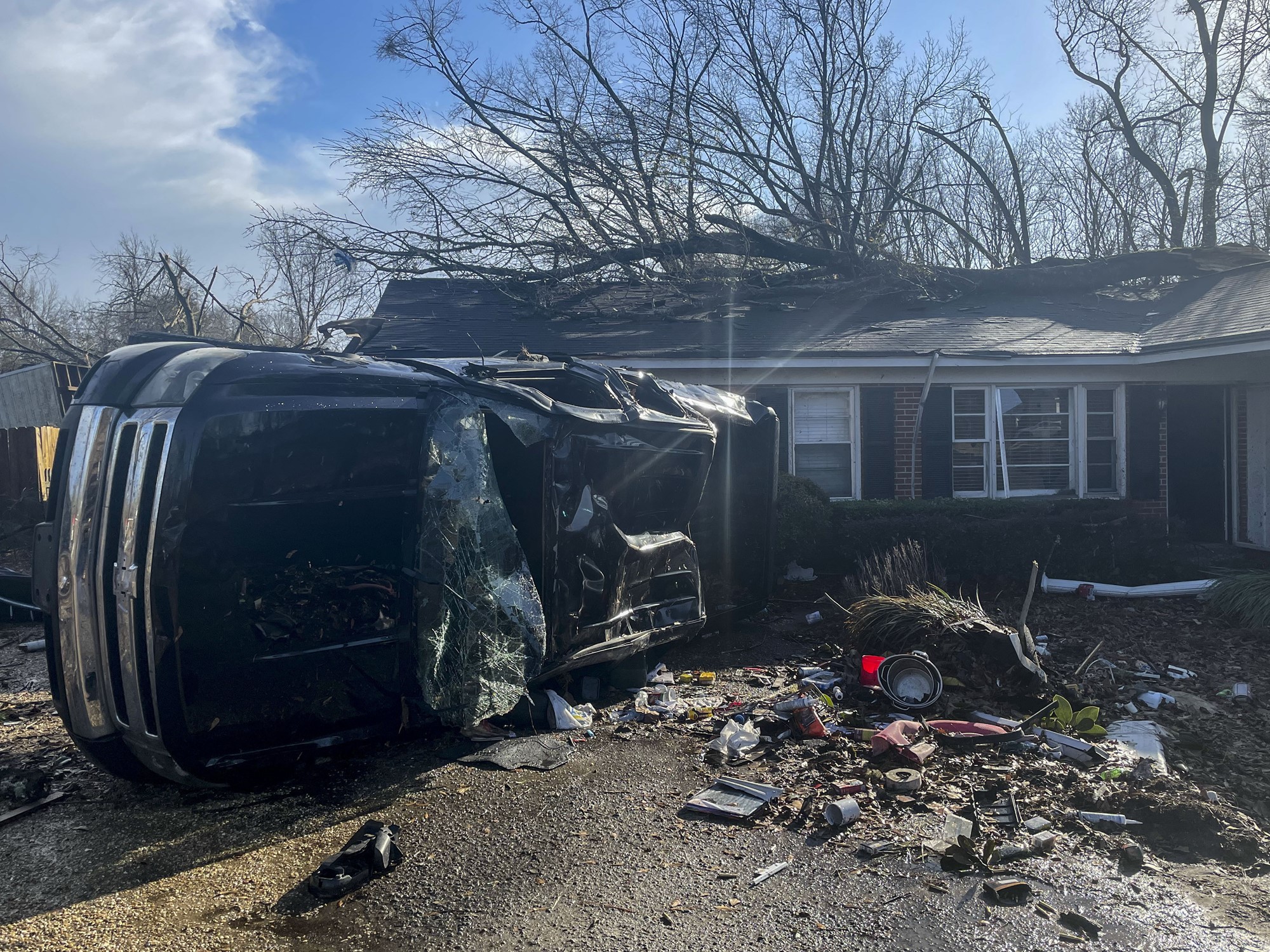A damaged car is pictured on its side in front of a home covered in debris.