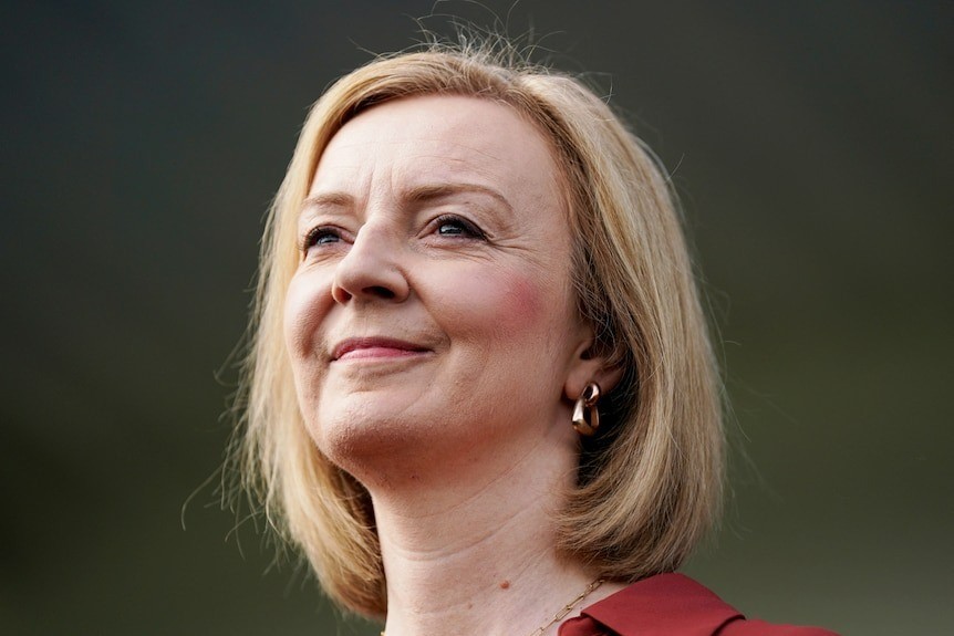 Liz Truss, with blonde hair and gold earrings, grins as she looks into the distance.