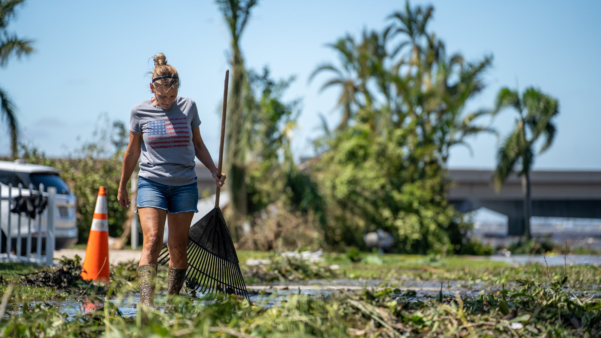 A woman holds a rake surrounded by green waste and debris.