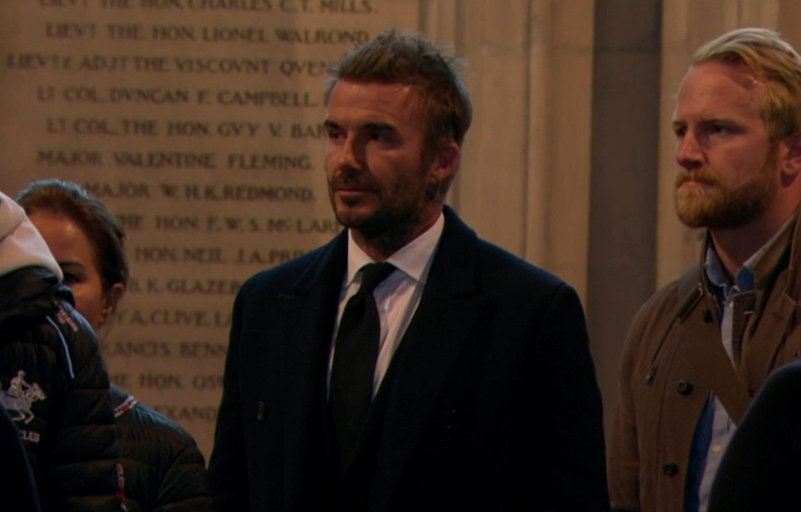 A man in a suit and tie stands in a hall.